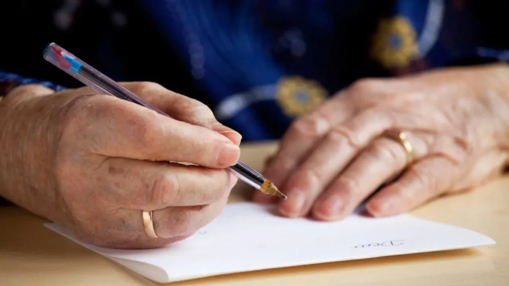 Manos de un adulto mayor escribiendo en un diario como parte de la estimulación cognitiva para adultos mayores.