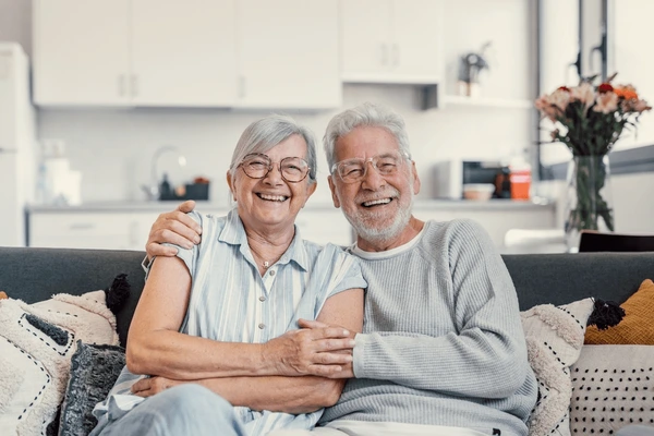 Pareja de adultos mayores sonriendo y disfrutando de un momento juntos en casa, reflejando bienestar y cuidado.